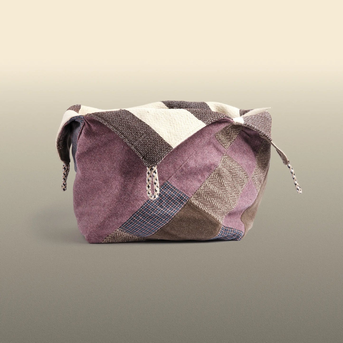 Homeware basket handmade from wool and cotton. One side is beige and brown and the other is colourful, with purple and grey as the most dominant colours.