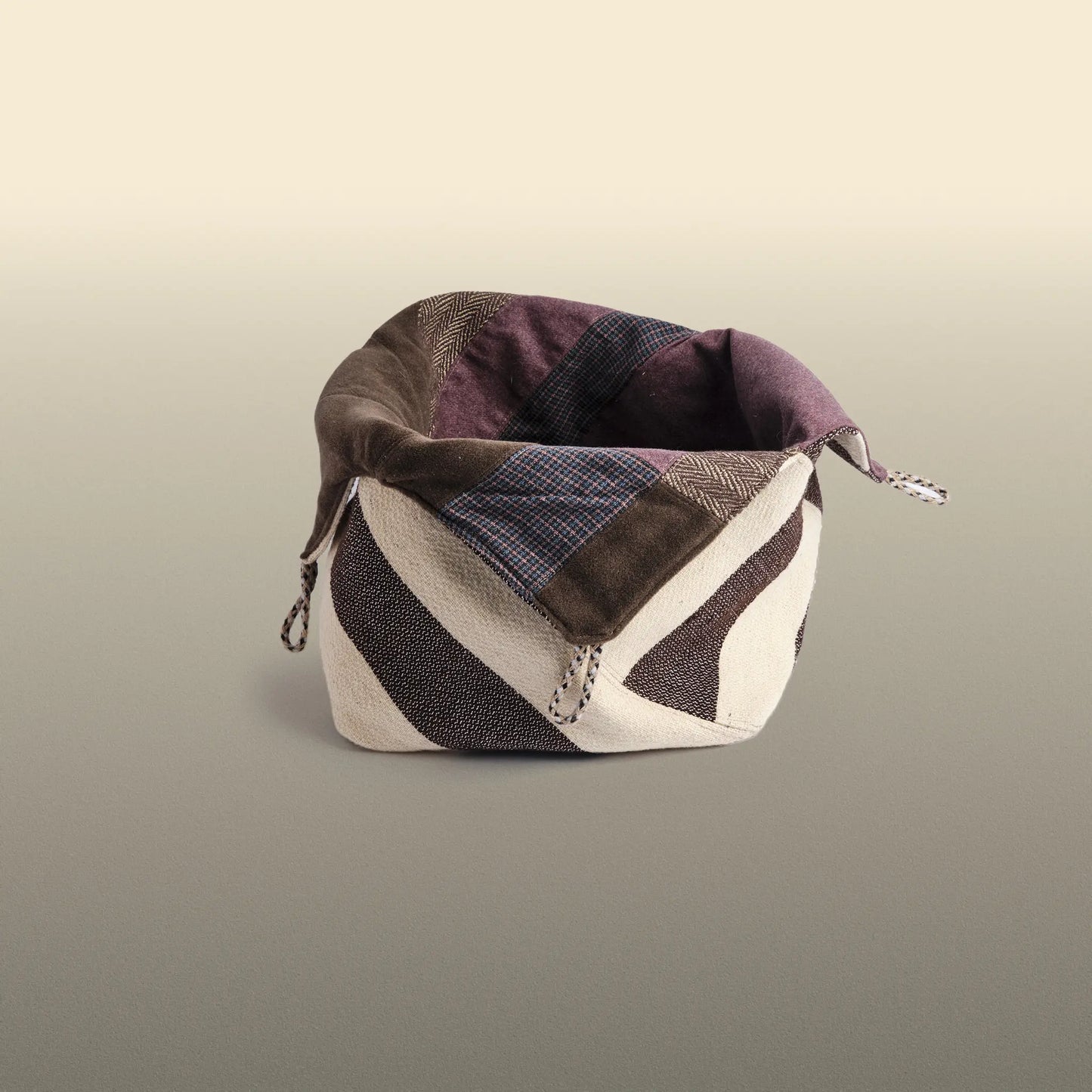 Homeware basket handmade from wool and cotton. One side is beige and brown and the other is colourful, with purple and grey as the most dominant colours.