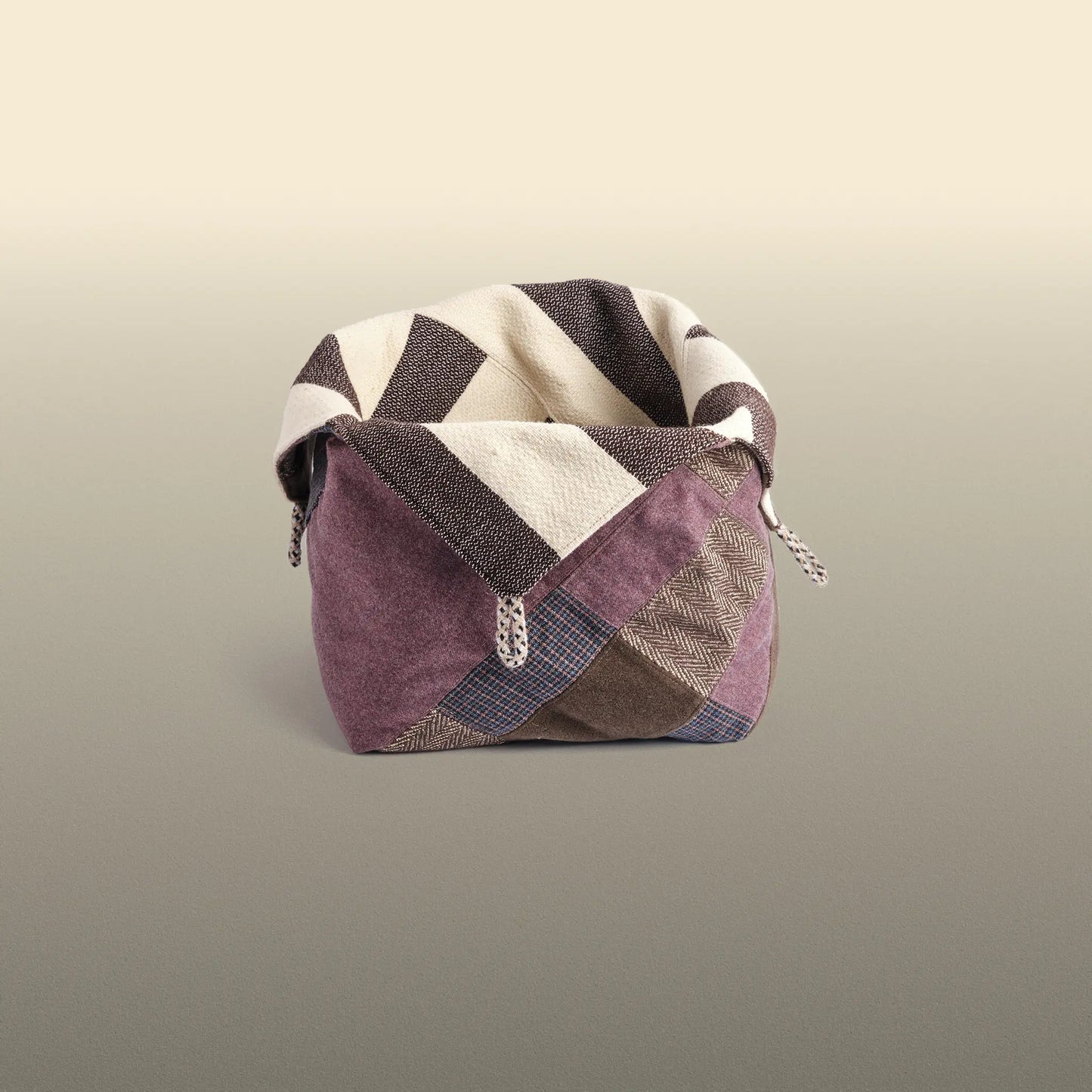 Homeware basket handmade from wool and cotton. One side is beige and brown and the other is colourful, with purple and grey as the most dominant colours.