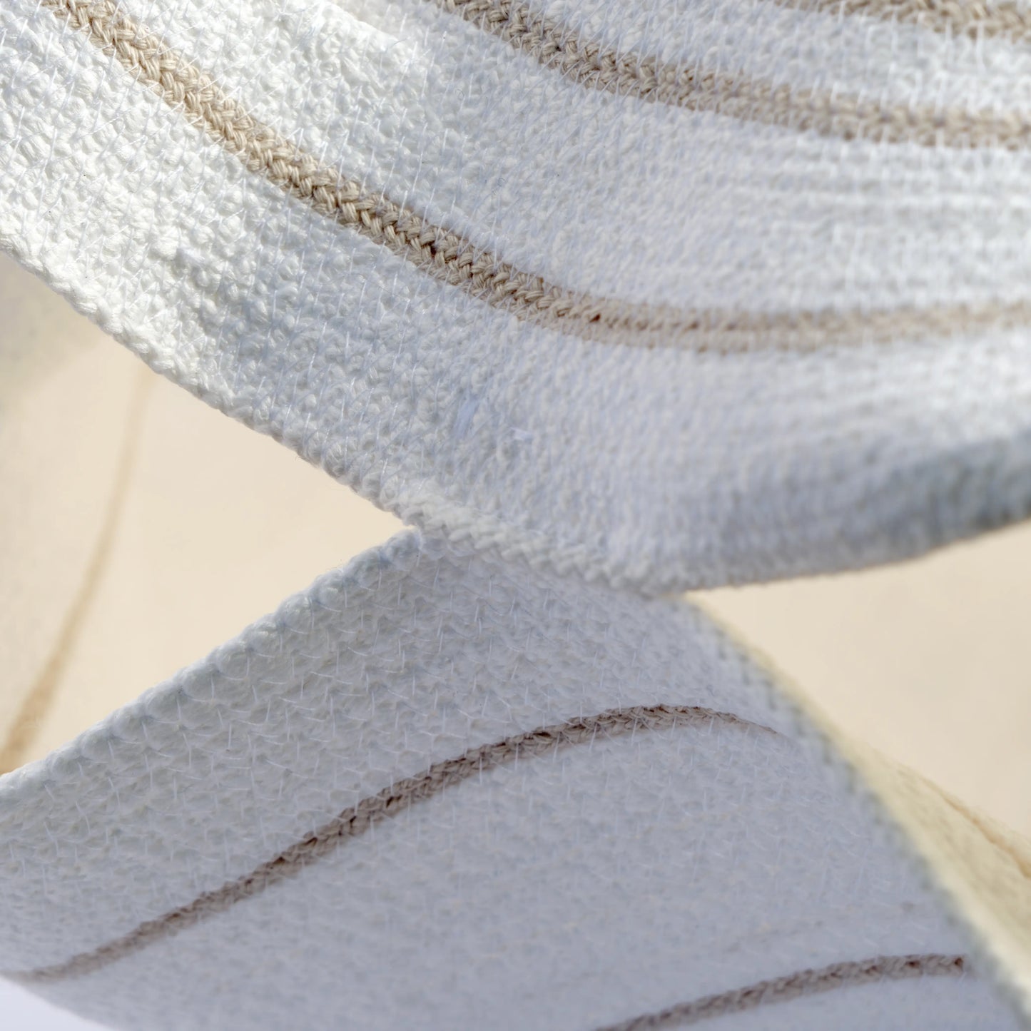 The image is a detail of a large chandelier handmade from cotton rope. It is white with beige details and decorative hanging rope.
