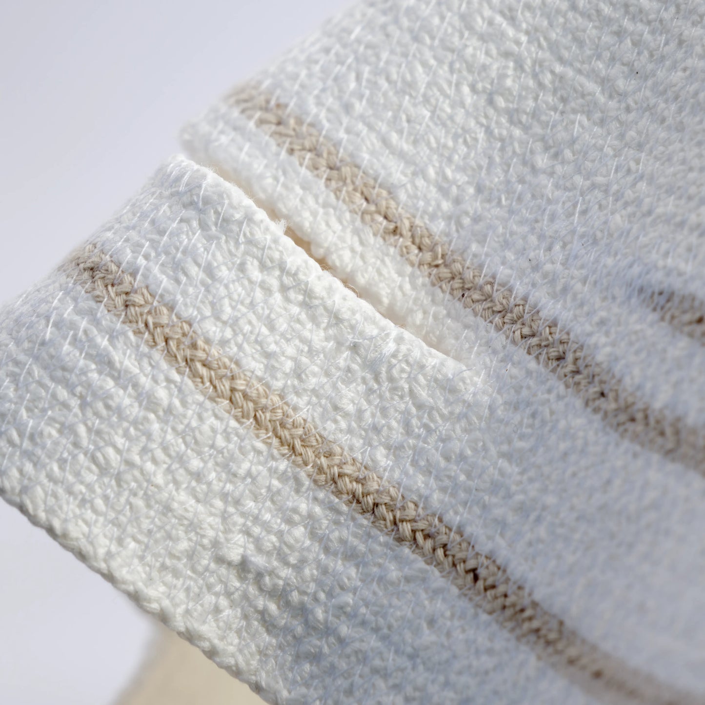 The image is a detail of a large chandelier handmade from cotton rope. It is white with beige details and decorative hanging rope.