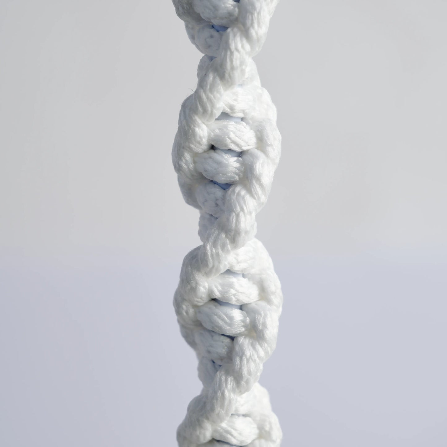 The image is a detail of a large chandelier handmade from cotton rope. It is white with beige details and decorative hanging rope.