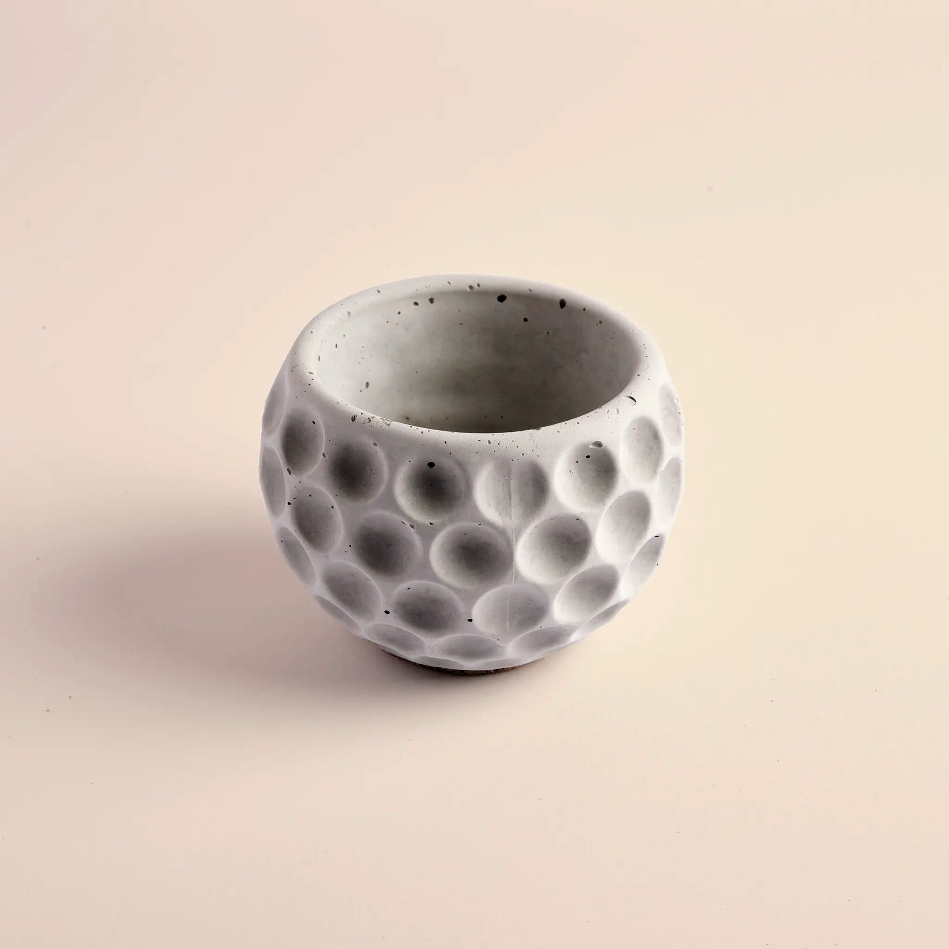 Small plant pot handmade from concrete. It is round with decorative circular dents.
