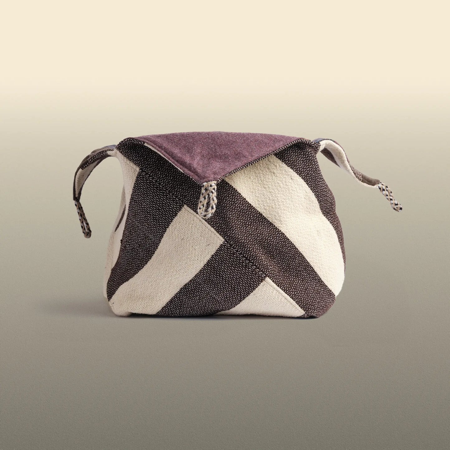 Homeware basket handmade from wool and cotton. One side is beige and brown and the other is colourful, with purple and grey as the most dominant colours. 