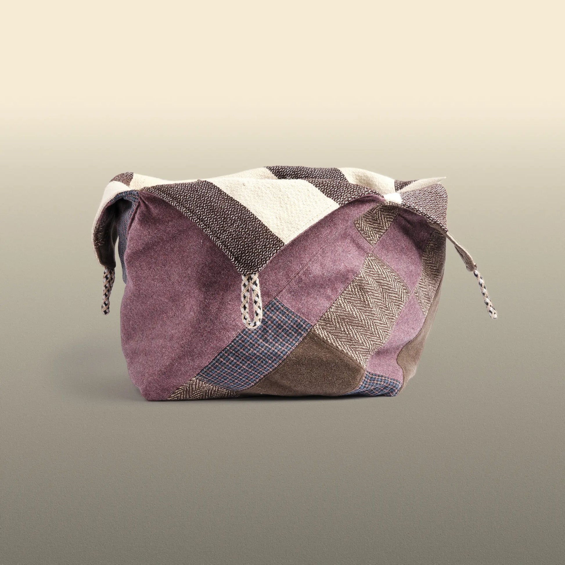 Homeware basket handmade from wool and cotton. One side is beige and brown and the other is colourful, with purple and grey as the most dominant colours. 