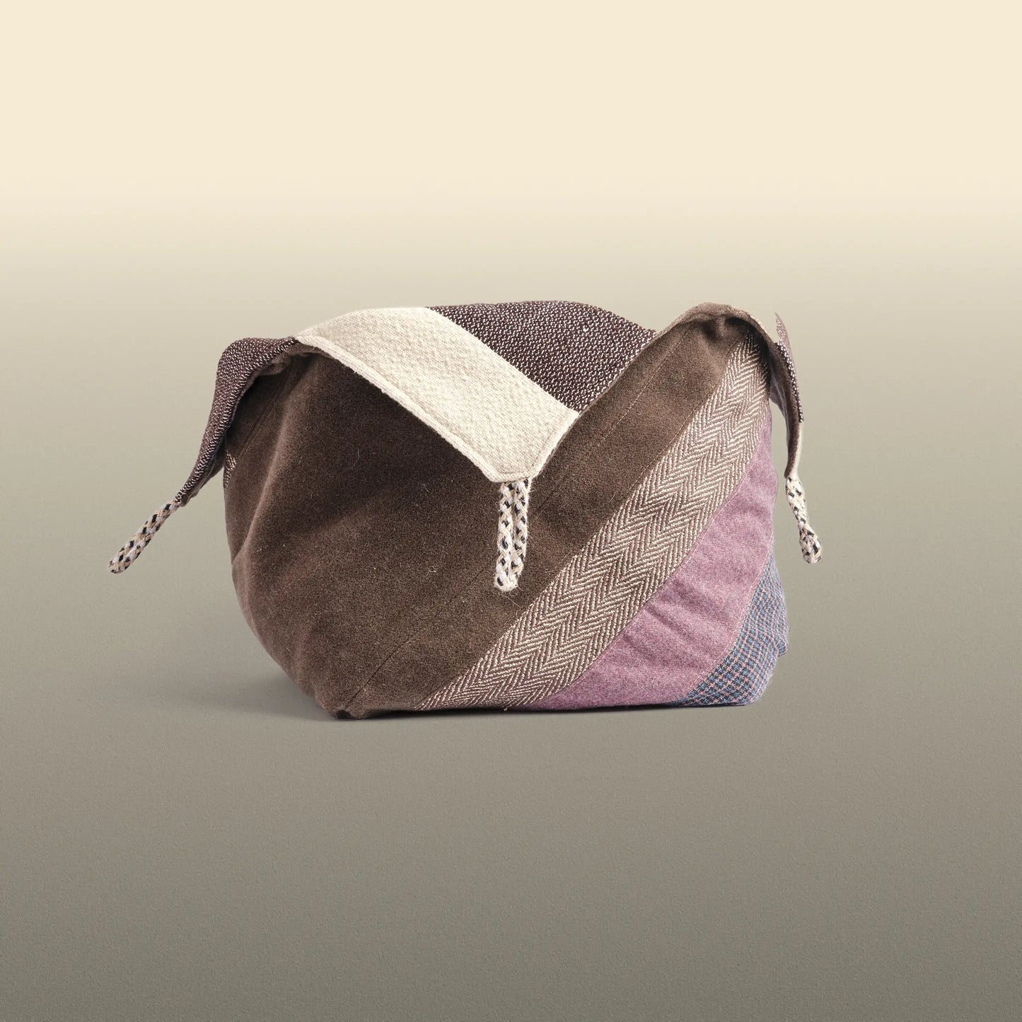 Homeware basket handmade from wool and cotton. One side is beige and brown and the other is colourful, with purple and grey as the most dominant colours. 