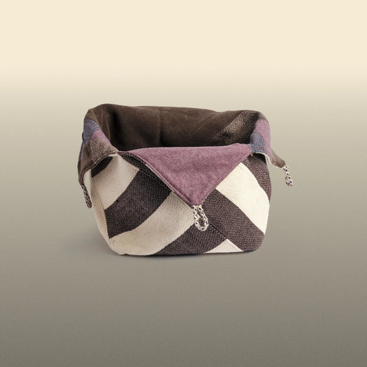 Homeware basket handmade from wool and cotton. One side is beige and brown and the other is colourful, with purple and grey as the most dominant colours. 