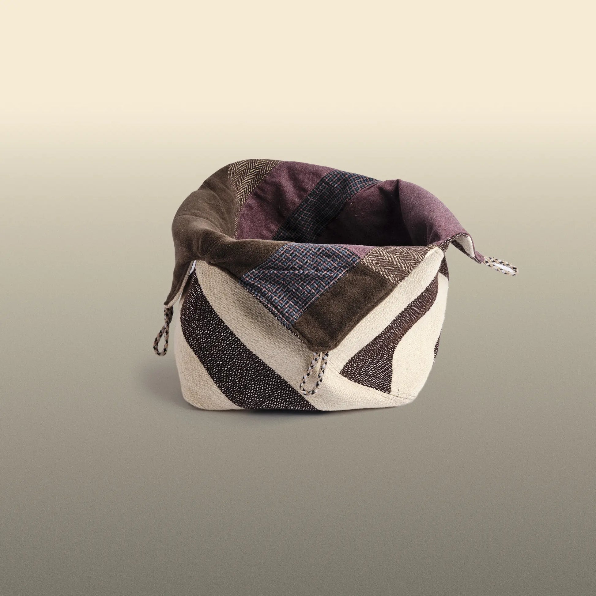 Homeware basket handmade from wool and cotton. One side is beige and brown and the other is colourful, with purple and grey as the most dominant colours. 