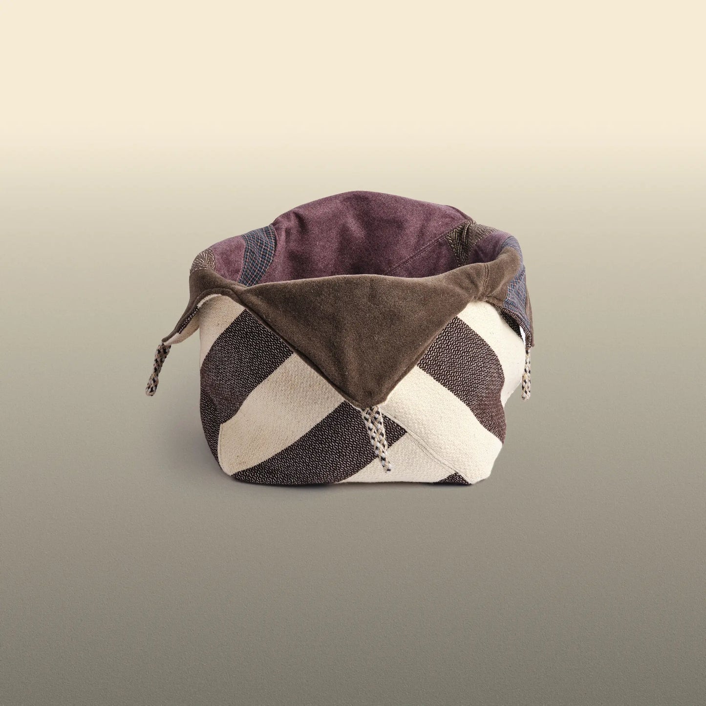Homeware basket handmade from wool and cotton. One side is beige and brown and the other is colourful, with purple and grey as the most dominant colours. 