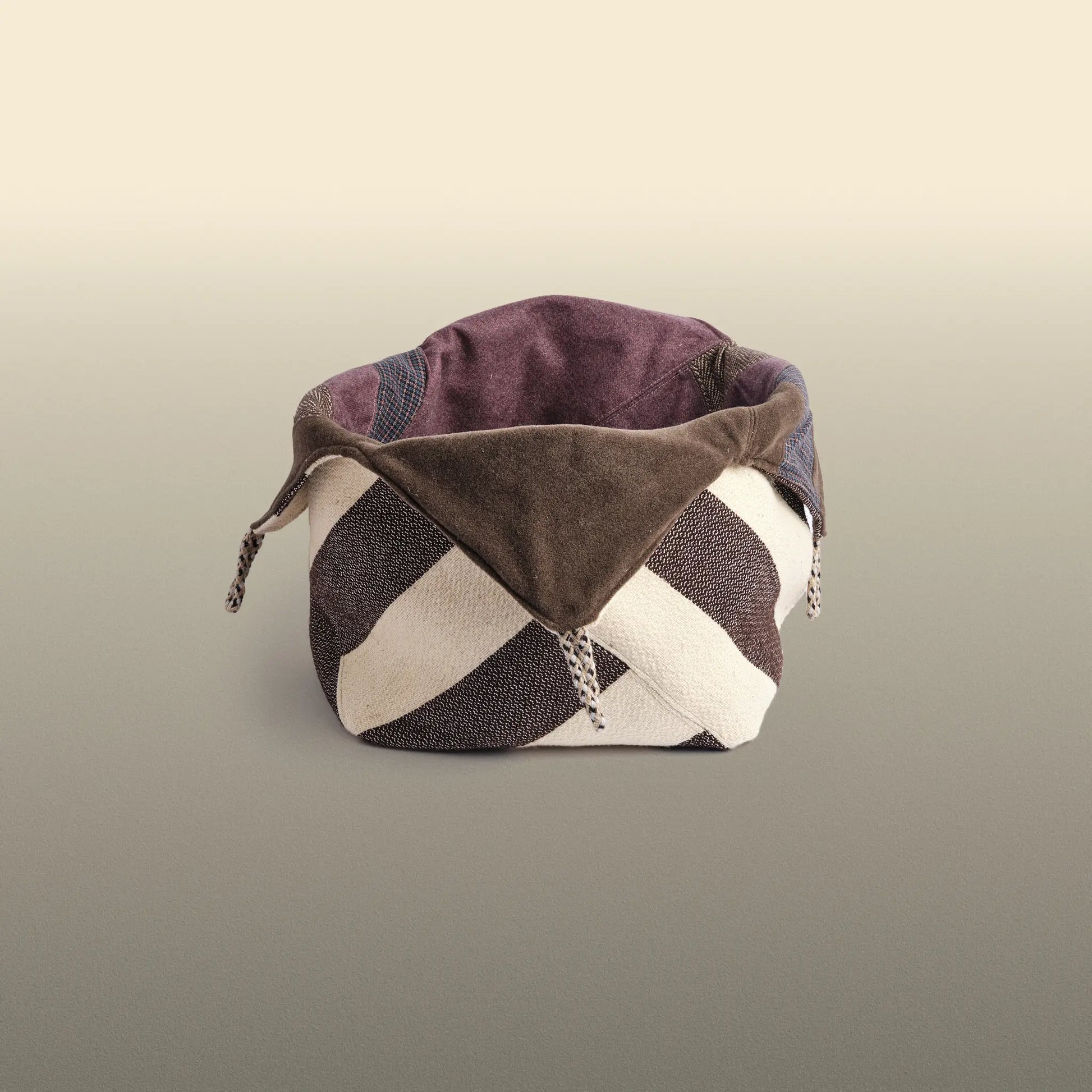 Homeware basket handmade from wool and cotton. One side is beige and brown and the other is colourful, with purple and grey as the most dominant colours. 