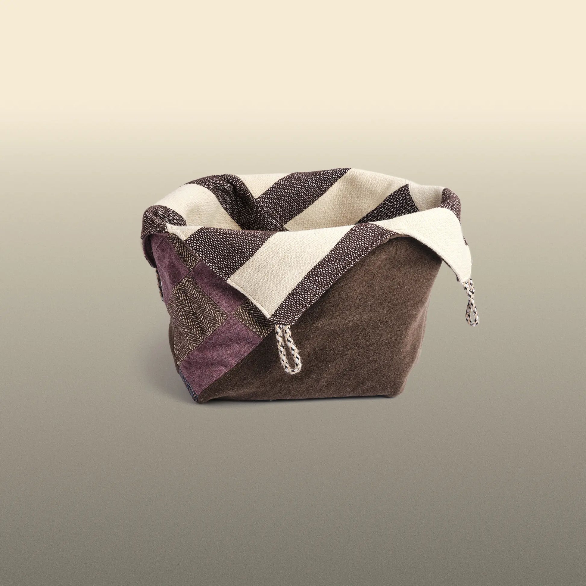 Homeware basket handmade from wool and cotton. One side is beige and brown and the other is colourful, with purple and grey as the most dominant colours. 