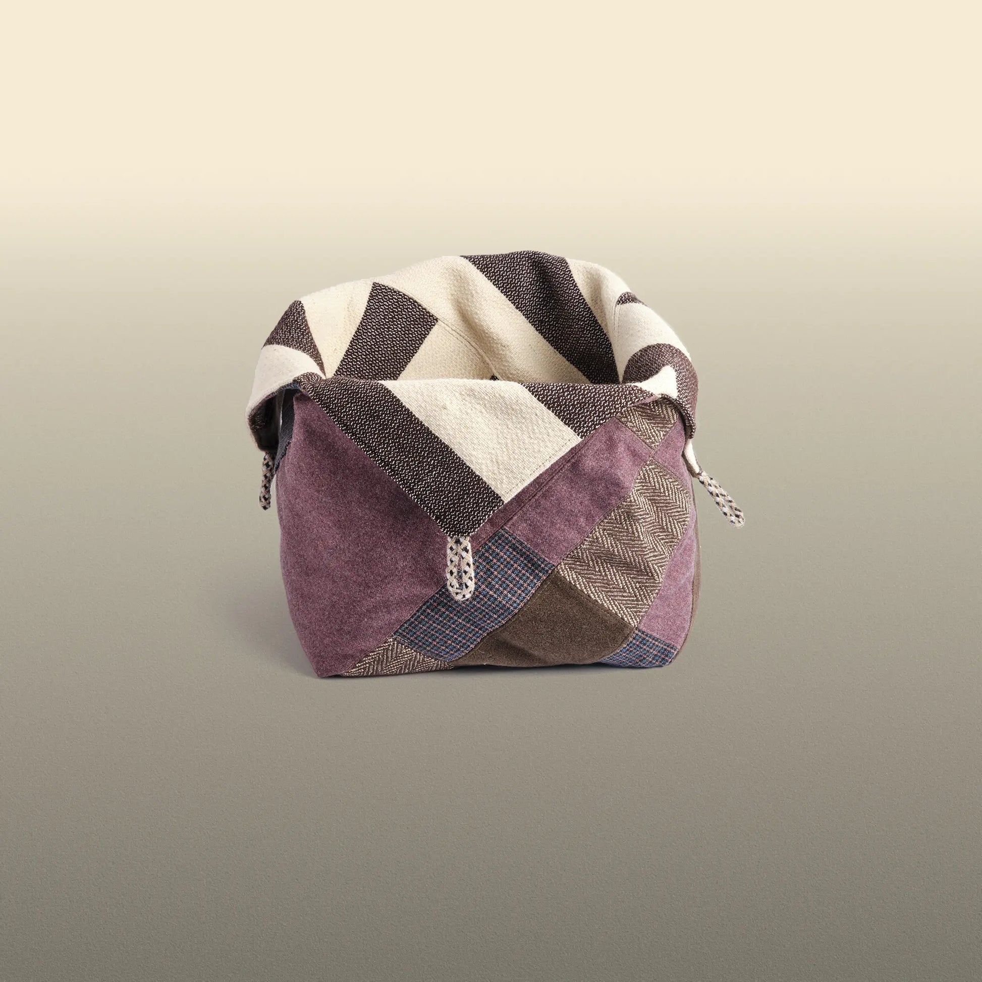 Homeware basket handmade from wool and cotton. One side is beige and brown and the other is colourful, with purple and grey as the most dominant colours. 
