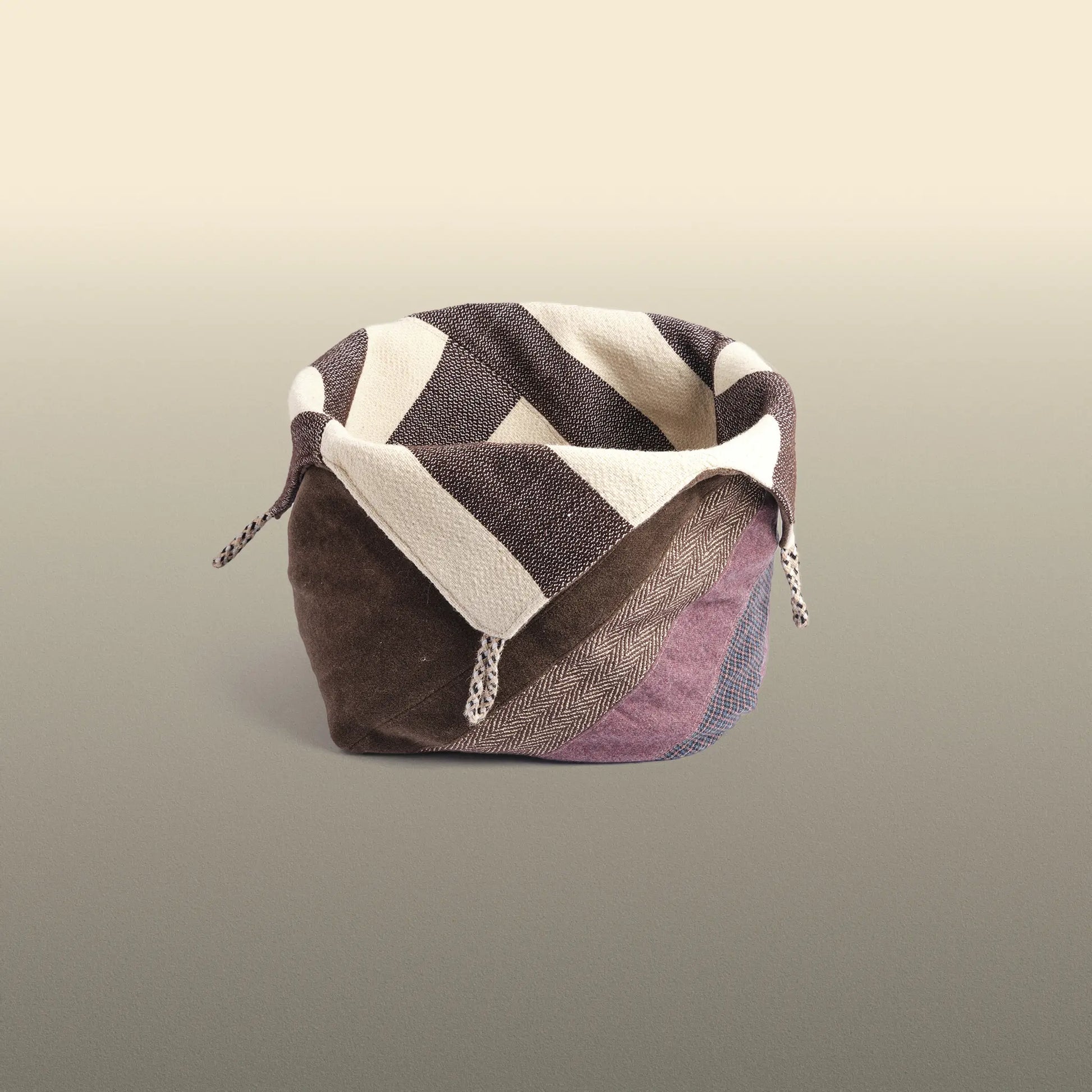 Homeware basket handmade from wool and cotton. One side is beige and brown and the other is colourful, with purple and grey as the most dominant colours. 