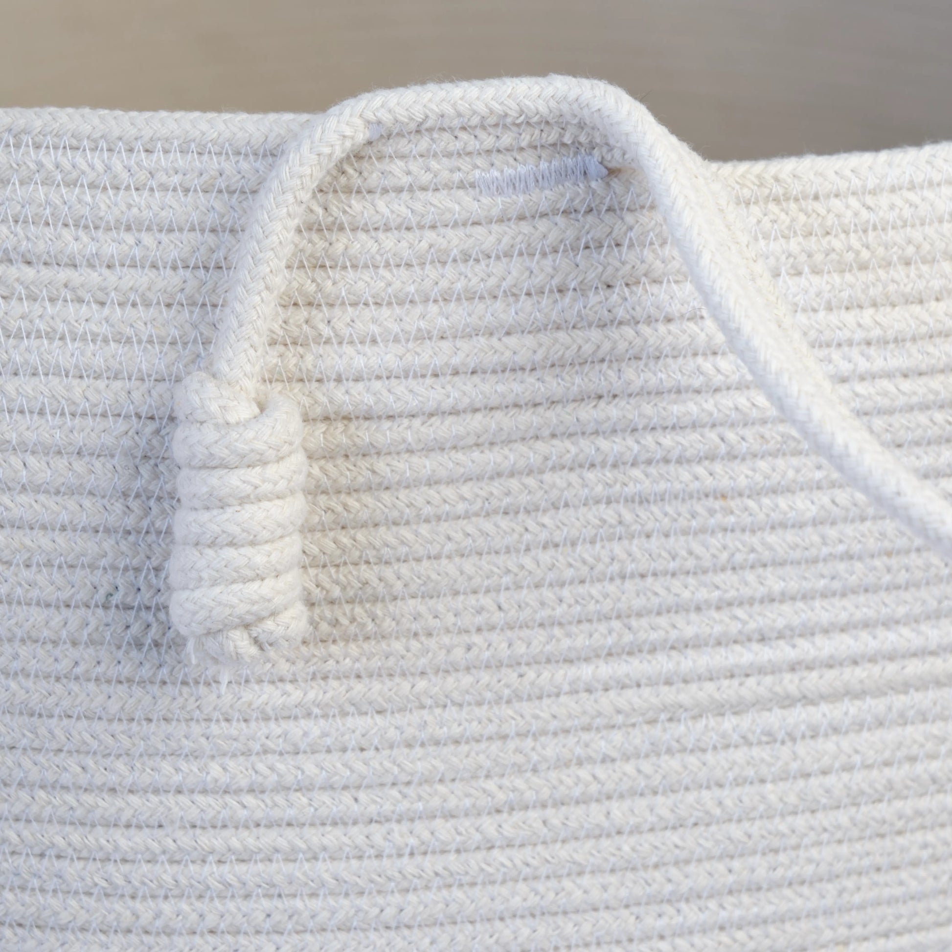 Homeware basket handmade from white cotton. The basket is round and has two handles. The image is a detail of the handles. 